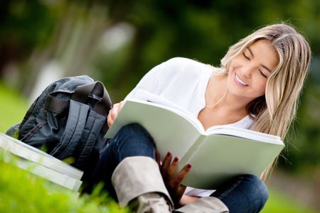 Casual young woman studying at the park holding a book