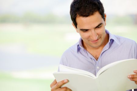 Casual man reading a book outdoors and smiling