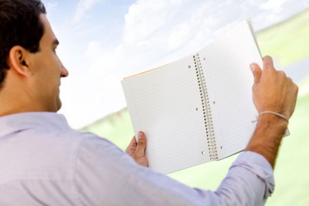 Male student reading a notebook outdoors - view from the back