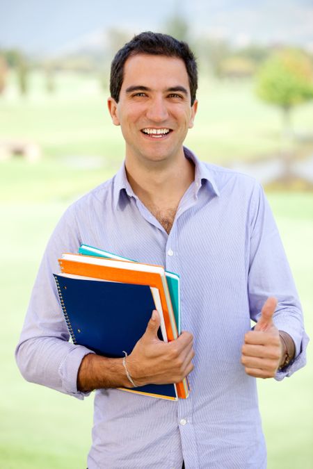 Happy male student with thumbs up holding a notebook