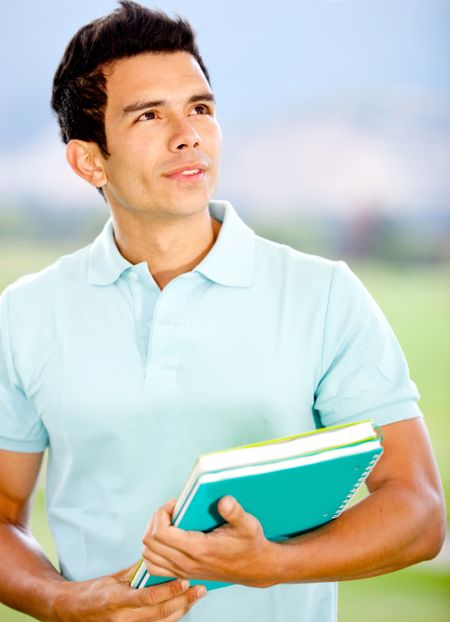 Thoughtful male student holding notebooks and looking up