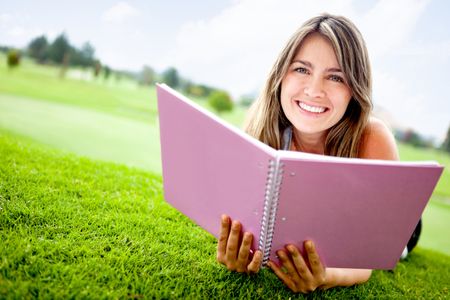 Female student lying at the park with a notebook
