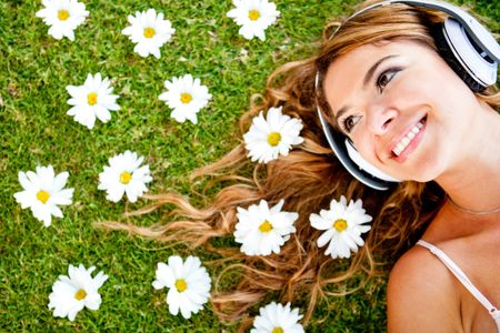 Beautiful woman listening to music with headphones lying outdoors