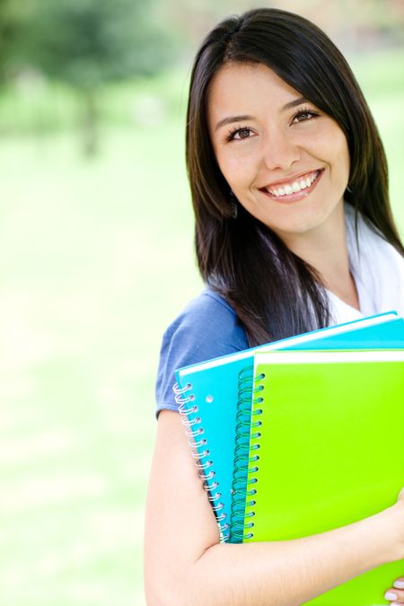 Young female student smiling and holding notebooks - outdoors