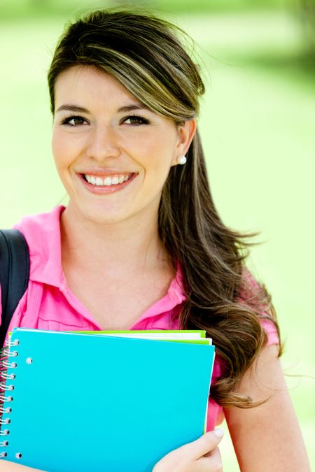 Portrait of a female student holding notebooks at the park