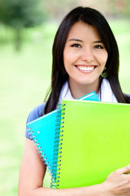 Happy female student holding notebooks and smiling outdoors