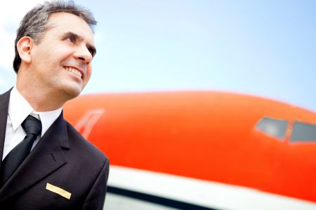 Portrait of a handsome pilot looking at the sky with an airplane at the background