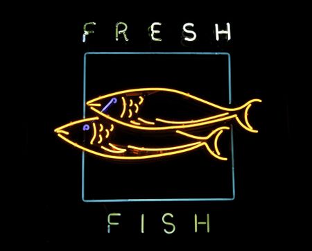 Neon sign in display window of restaurant that serves fresh fish, with black background