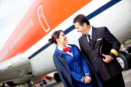 Pilot and flight attendant at the airport with an airplane at the background