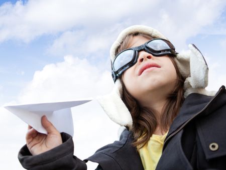 Young boy pilot holding a paper airplane looking at the sky