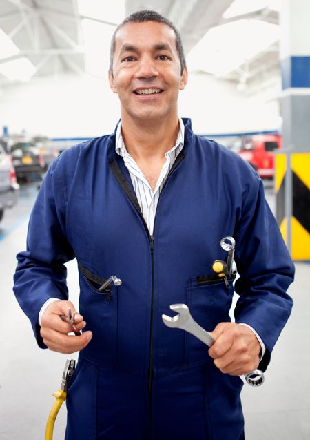 Male mechanic holding tools at a car garage and smiling