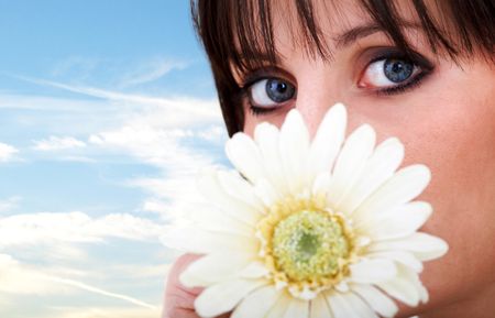 girl with a daisy by her face and a blue sky in the background