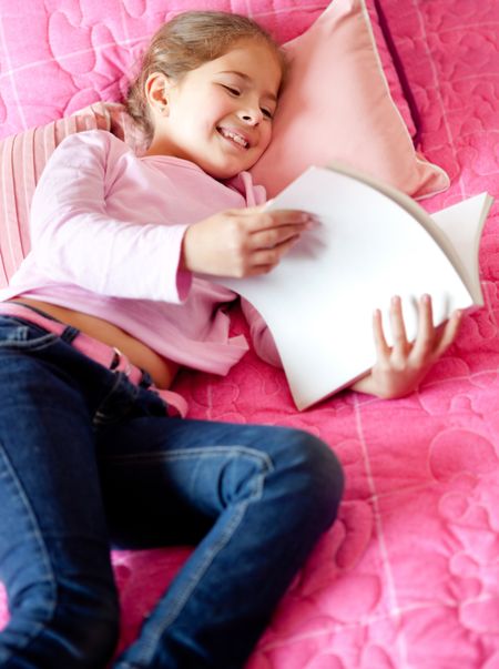 Cute little girl reading a book in bed
