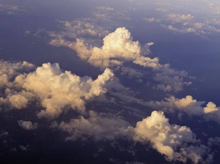 Aerial view at sunset: Tops of cumulus clouds seen from 30,000 feet or higher over land